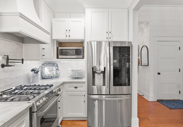 kitchen with white cabinetry, light stone counters, light hardwood / wood-style flooring, appliances with stainless steel finishes, and custom range hood