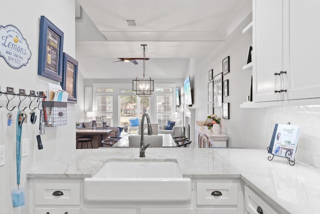 kitchen featuring sink, light stone counters, a notable chandelier, white cabinets, and decorative light fixtures