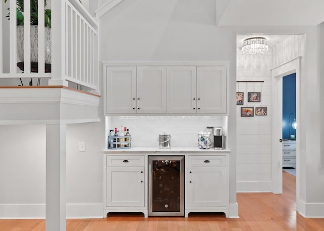 bar with wine cooler, backsplash, white cabinetry, and light hardwood / wood-style floors