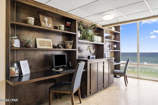 office featuring a paneled ceiling, built in desk, a wall of windows, and built in shelves