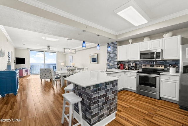 kitchen featuring hanging light fixtures, appliances with stainless steel finishes, white cabinets, and kitchen peninsula