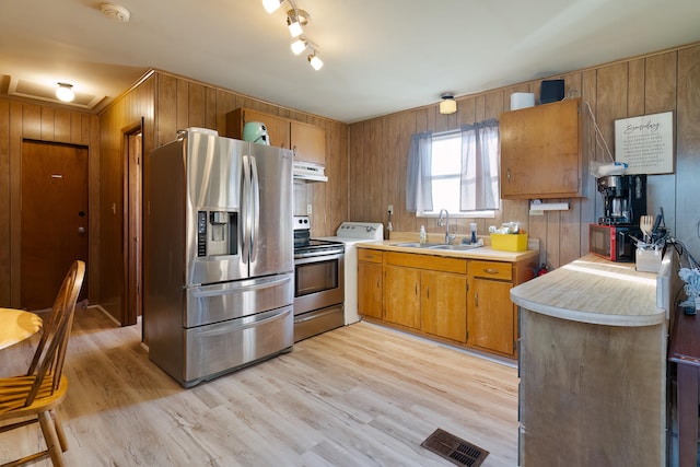 kitchen featuring rail lighting, sink, wooden walls, stainless steel appliances, and light hardwood / wood-style floors