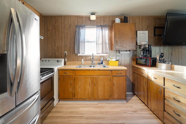 kitchen featuring sink, light hardwood / wood-style flooring, wooden walls, and appliances with stainless steel finishes