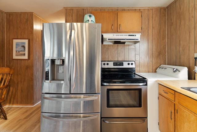 kitchen with appliances with stainless steel finishes, wooden walls, and light hardwood / wood-style floors