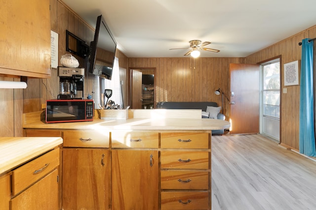 kitchen featuring ceiling fan, kitchen peninsula, wood walls, and light wood-type flooring