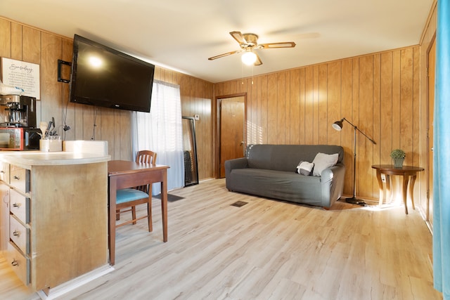 living room featuring light hardwood / wood-style flooring, wooden walls, and ceiling fan