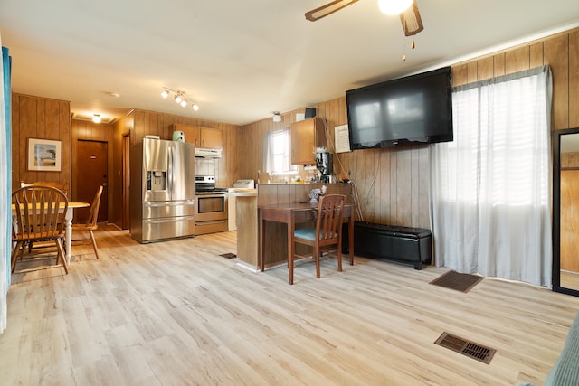 kitchen featuring ceiling fan, stainless steel appliances, light hardwood / wood-style floors, kitchen peninsula, and wood walls