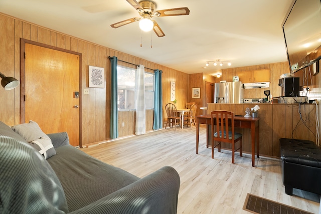 living room featuring ceiling fan, light hardwood / wood-style floors, and wood walls