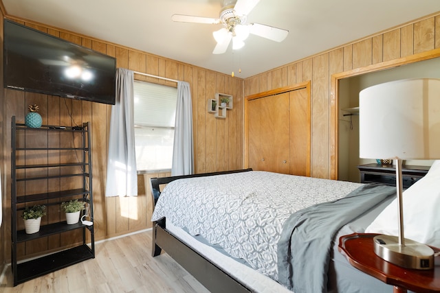 bedroom with a closet, light hardwood / wood-style floors, ceiling fan, and wood walls