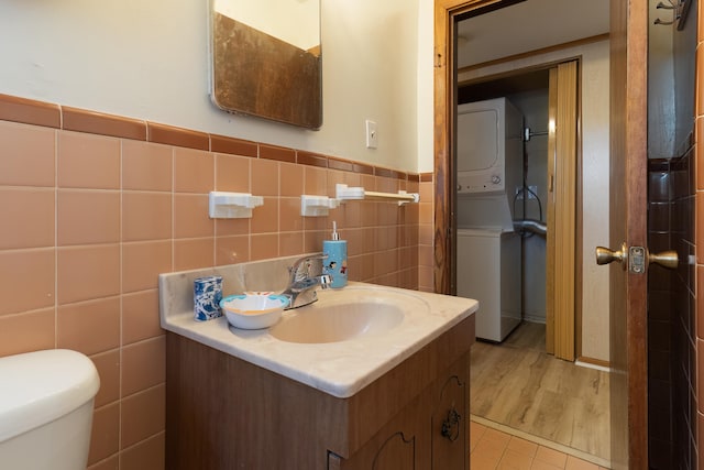 bathroom featuring stacked washer and dryer, vanity, toilet, and tile walls