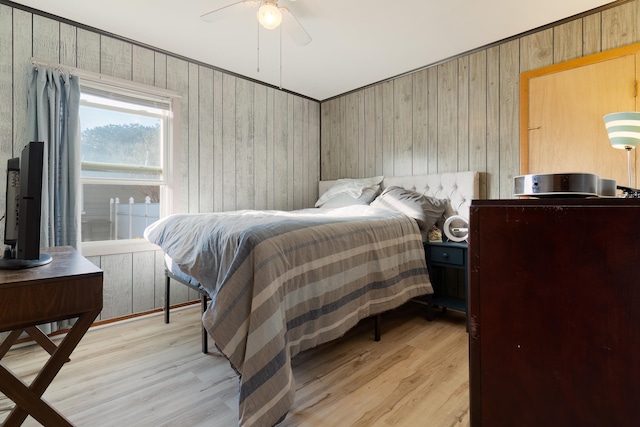 bedroom with ceiling fan, light wood-type flooring, and wood walls