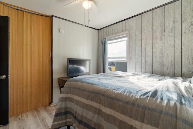 bedroom featuring crown molding, light hardwood / wood-style floors, ceiling fan, and wood walls