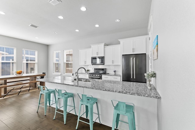 kitchen featuring light stone countertops, stainless steel appliances, a breakfast bar, and white cabinets