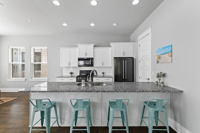 kitchen with white cabinetry, high quality fridge, a kitchen bar, and dark stone counters