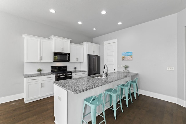 kitchen with high quality fridge, white cabinets, a kitchen bar, and black range with gas cooktop