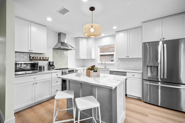 kitchen with wall chimney exhaust hood, a center island, appliances with stainless steel finishes, light stone countertops, and white cabinets