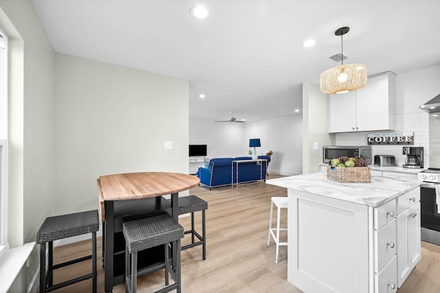 kitchen featuring a kitchen island, white cabinetry, backsplash, light hardwood / wood-style floors, and light stone countertops