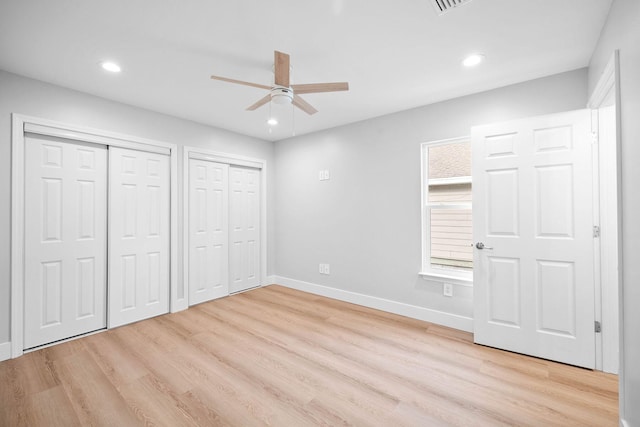 unfurnished bedroom featuring ceiling fan, light hardwood / wood-style flooring, and multiple closets