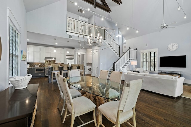 dining room with washer / dryer, dark wood-type flooring, ceiling fan with notable chandelier, and high vaulted ceiling