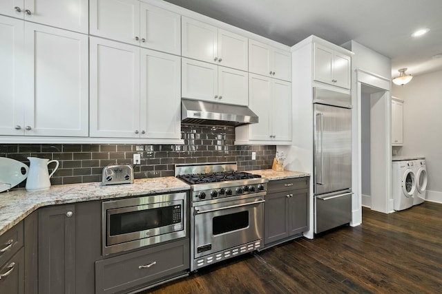 kitchen featuring range hood, independent washer and dryer, built in appliances, light stone counters, and white cabinets