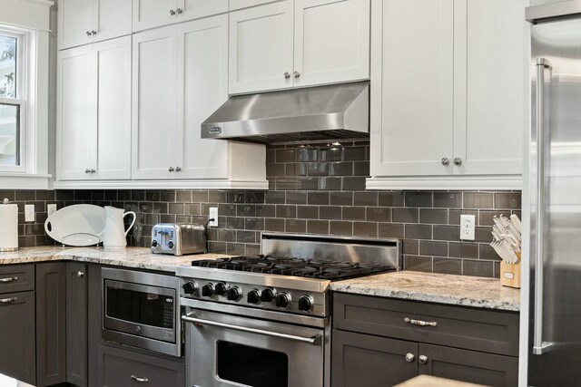 kitchen featuring extractor fan, appliances with stainless steel finishes, white cabinets, decorative backsplash, and light stone countertops