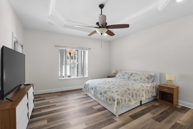 bedroom with a raised ceiling, crown molding, dark wood-type flooring, and ceiling fan