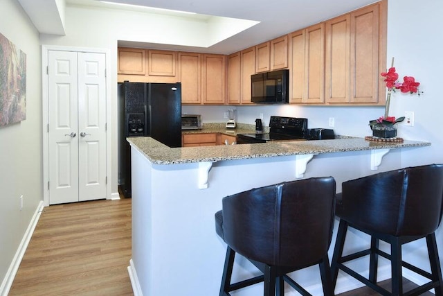 kitchen with light hardwood / wood-style flooring, a kitchen breakfast bar, kitchen peninsula, light stone countertops, and black appliances