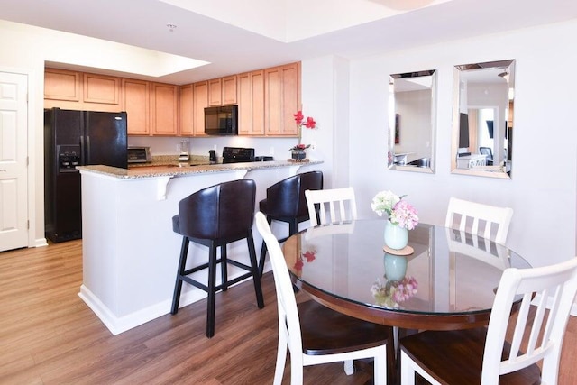 kitchen with a breakfast bar, black appliances, hardwood / wood-style flooring, kitchen peninsula, and light stone countertops