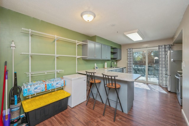 kitchen with sink, a breakfast bar, fridge, dark hardwood / wood-style floors, and kitchen peninsula