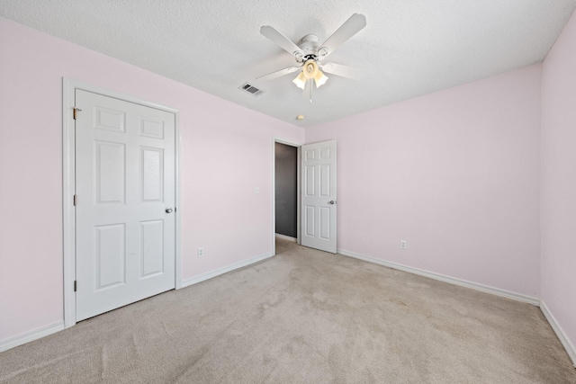 unfurnished bedroom with ceiling fan, light colored carpet, and a textured ceiling