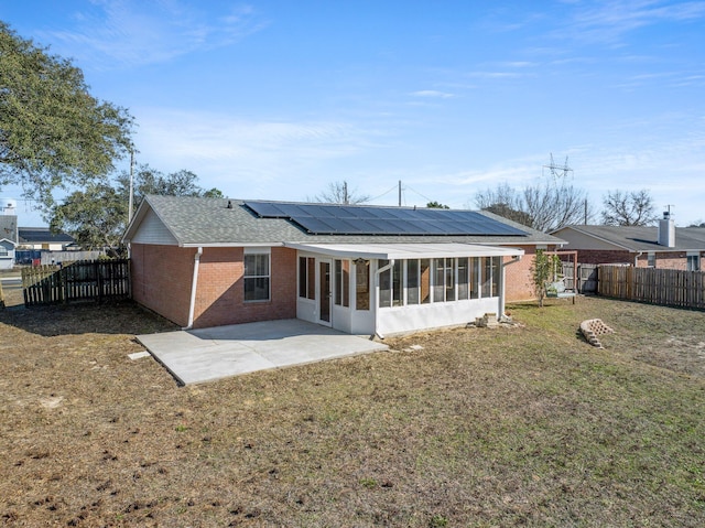 back of house with a lawn, a sunroom, a patio, and solar panels