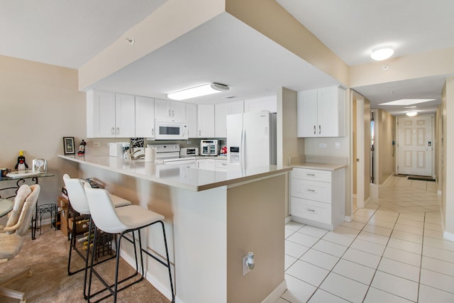 kitchen with a kitchen bar, light tile patterned floors, kitchen peninsula, white appliances, and white cabinets