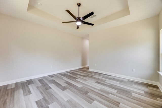 spare room with ceiling fan, a raised ceiling, and light wood-type flooring