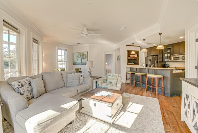 living room with ceiling fan, ornamental molding, and light wood-type flooring