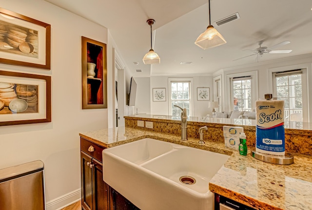 kitchen featuring sink, ceiling fan, light stone counters, ornamental molding, and decorative light fixtures