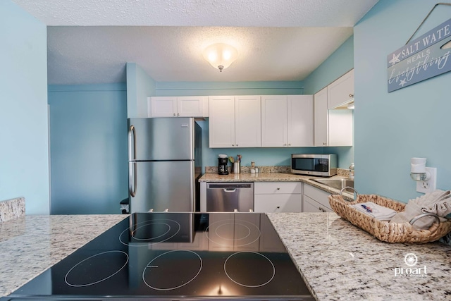 kitchen with stainless steel appliances, light stone countertops, a textured ceiling, and white cabinets