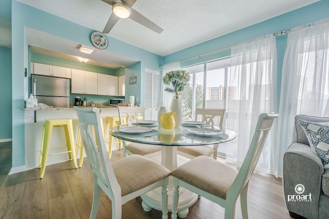 dining space with ceiling fan, a textured ceiling, and light hardwood / wood-style floors