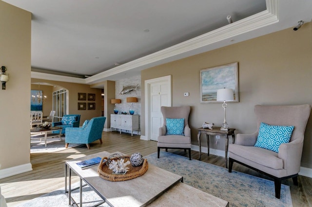 living room with hardwood / wood-style flooring, ornamental molding, a raised ceiling, and a chandelier