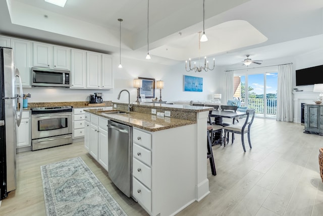 kitchen featuring pendant lighting, stainless steel appliances, a tray ceiling, white cabinets, and a center island with sink