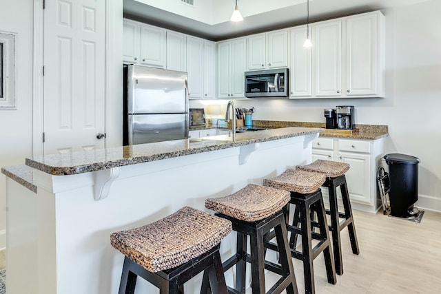 kitchen with hanging light fixtures, white cabinetry, appliances with stainless steel finishes, and a kitchen bar