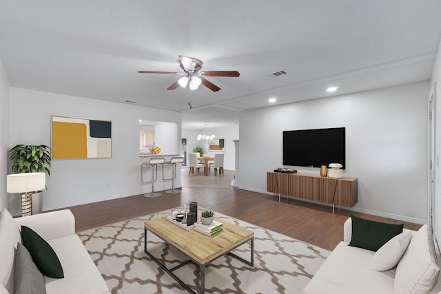 living room with ceiling fan with notable chandelier, hardwood / wood-style floors, and a textured ceiling