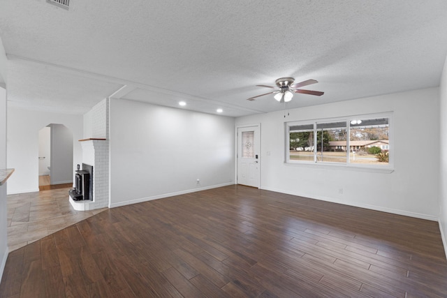 unfurnished living room with ceiling fan, dark hardwood / wood-style floors, a brick fireplace, and a textured ceiling