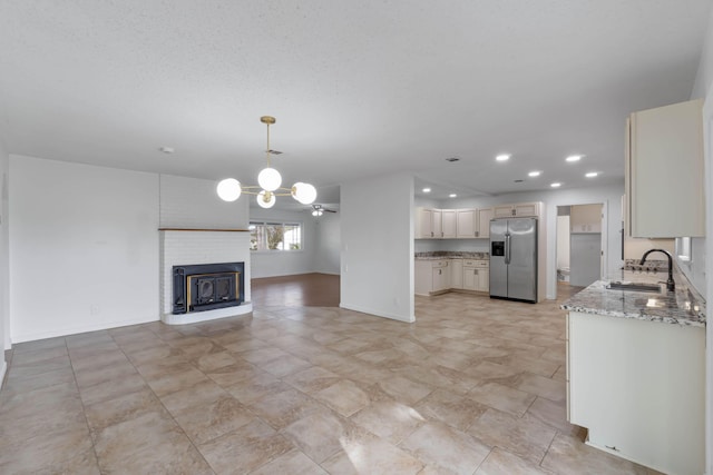 unfurnished living room featuring a fireplace, a chandelier, sink, and a textured ceiling