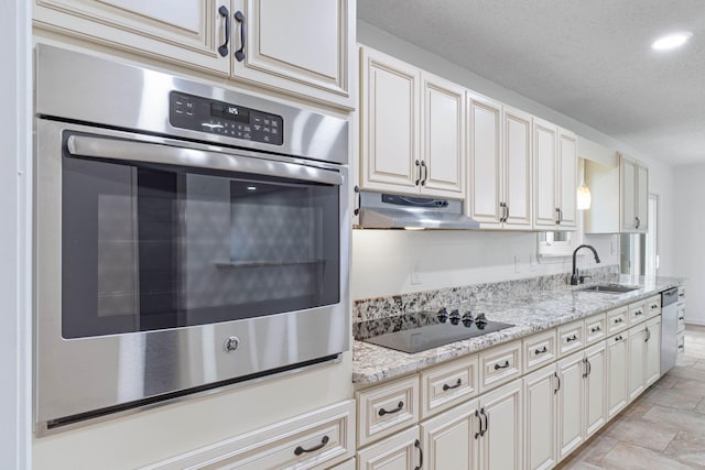 kitchen with sink, appliances with stainless steel finishes, light stone counters, cream cabinets, and a textured ceiling