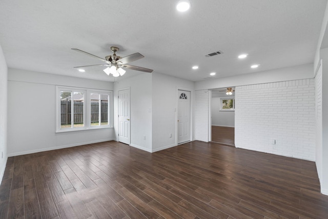 empty room featuring dark hardwood / wood-style flooring, a textured ceiling, ceiling fan, and brick wall