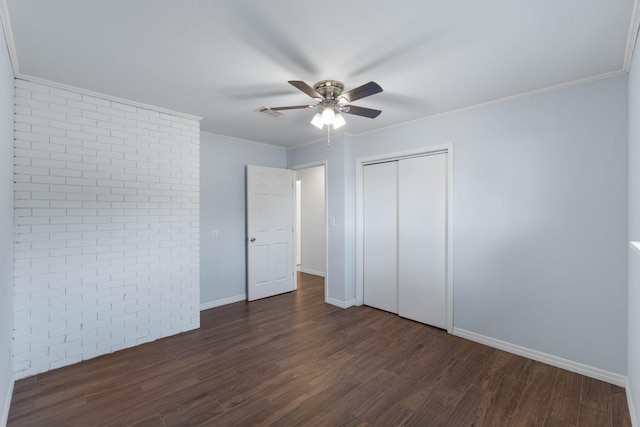 unfurnished bedroom with dark hardwood / wood-style flooring, ornamental molding, a closet, and brick wall