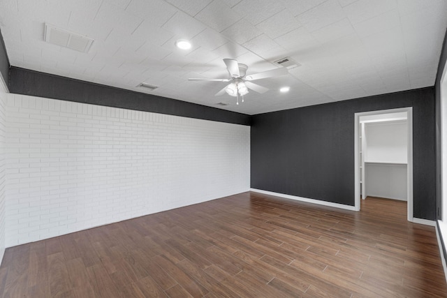 empty room with hardwood / wood-style floors, ceiling fan, and brick wall