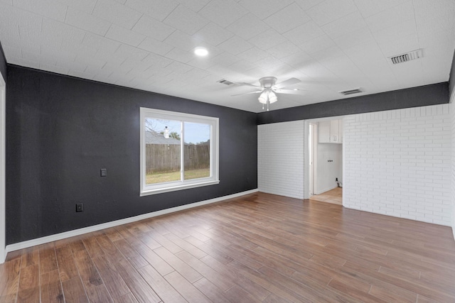 spare room with ceiling fan, brick wall, and light hardwood / wood-style floors