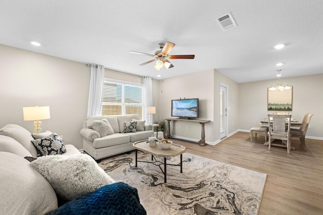 living room with ceiling fan with notable chandelier and light hardwood / wood-style floors