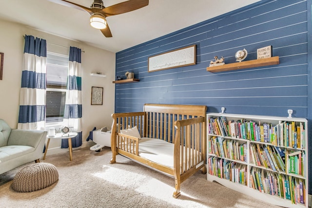 carpeted bedroom with a nursery area, ceiling fan, and wood walls